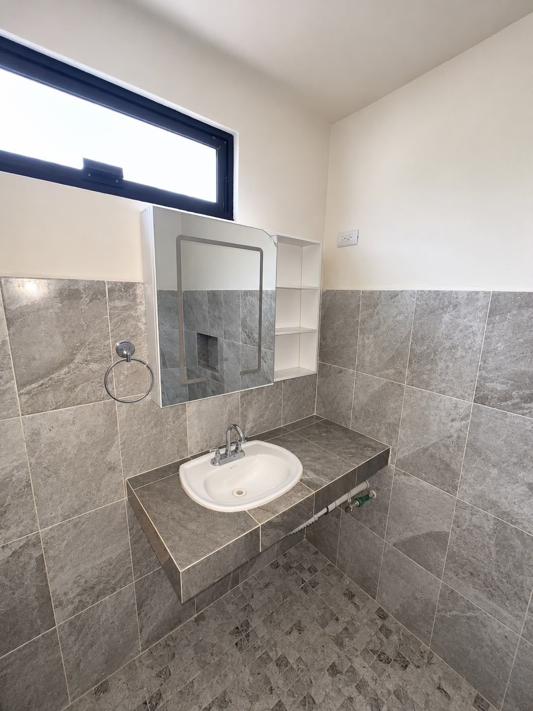 A bathroom with a white sink, a mirror, and grey tiled walls.