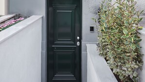 A black door with a small window above it, a white wall with a planter of green and yellow foliage, and a beige upper wall. - Presidential Suites by Athens Stay (Athens)