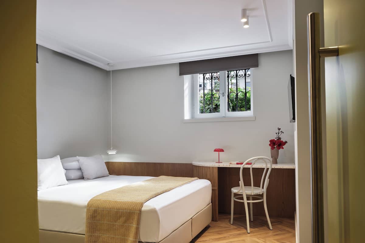 Una camera da letto con un letto, un comodino, una sedia, una finestra e vista sul verde.