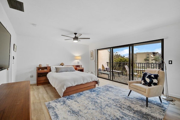 A bedroom with a bed, bedside tables, a desk, a chair, a large window, and a balcony with outdoor furniture. - Modern Siesta Key Condo: Family-Friendly Retreat at Midnight Cove II 424D (Siesta Key)