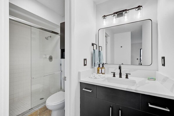 Un baño moderno con cabina de ducha de vidrio, inodoro blanco, tocador con espejo y lavabo.
