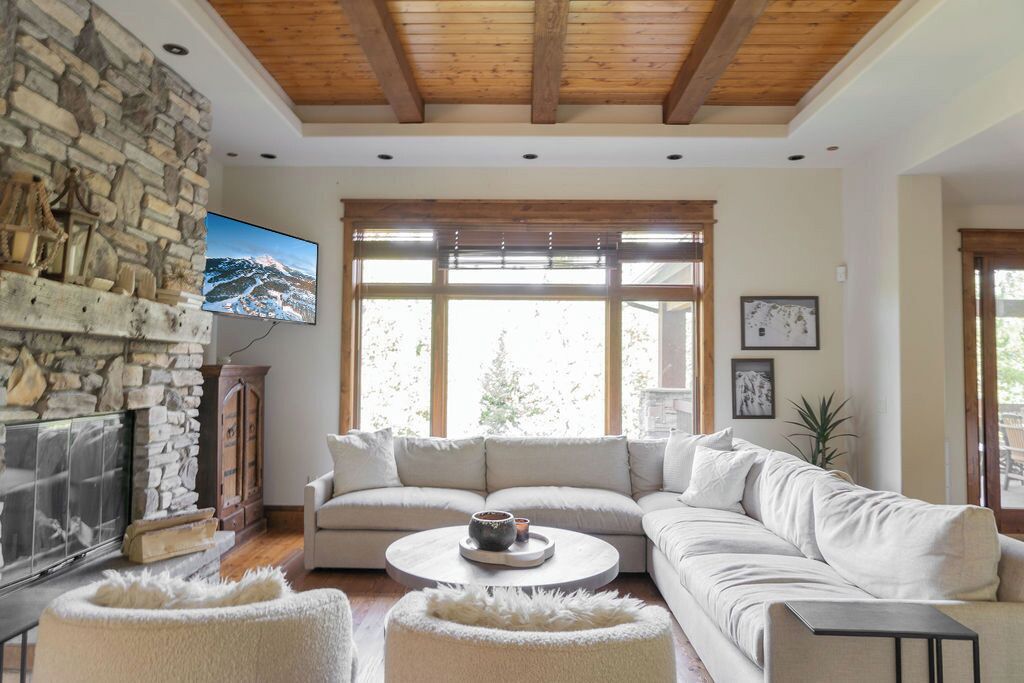 A cozy living room with a stone fireplace, a large window with blinds, a beige sofa, and a round coffee table.