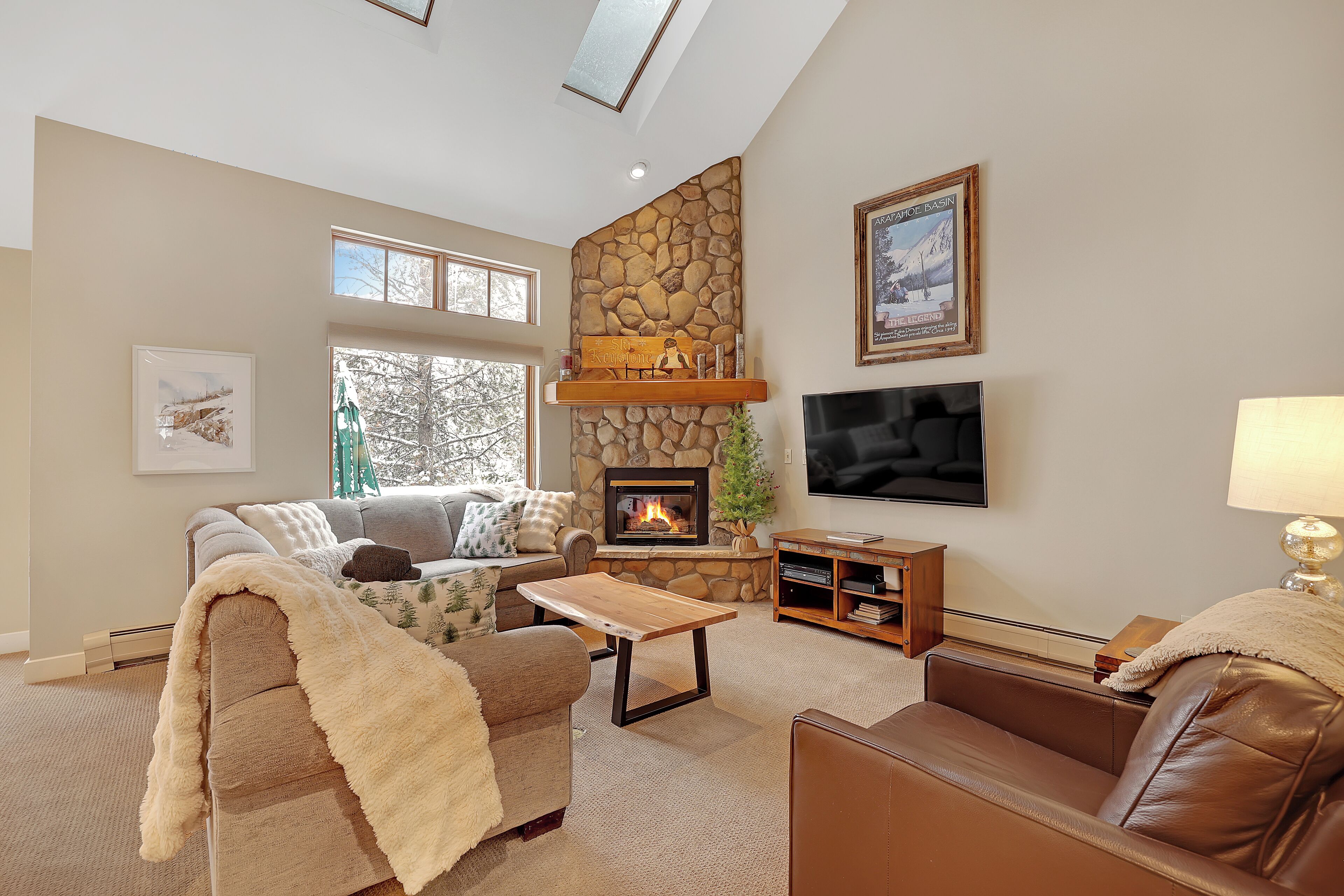 A cozy living room with a stone fireplace, a flat-screen TV, and comfortable seating.