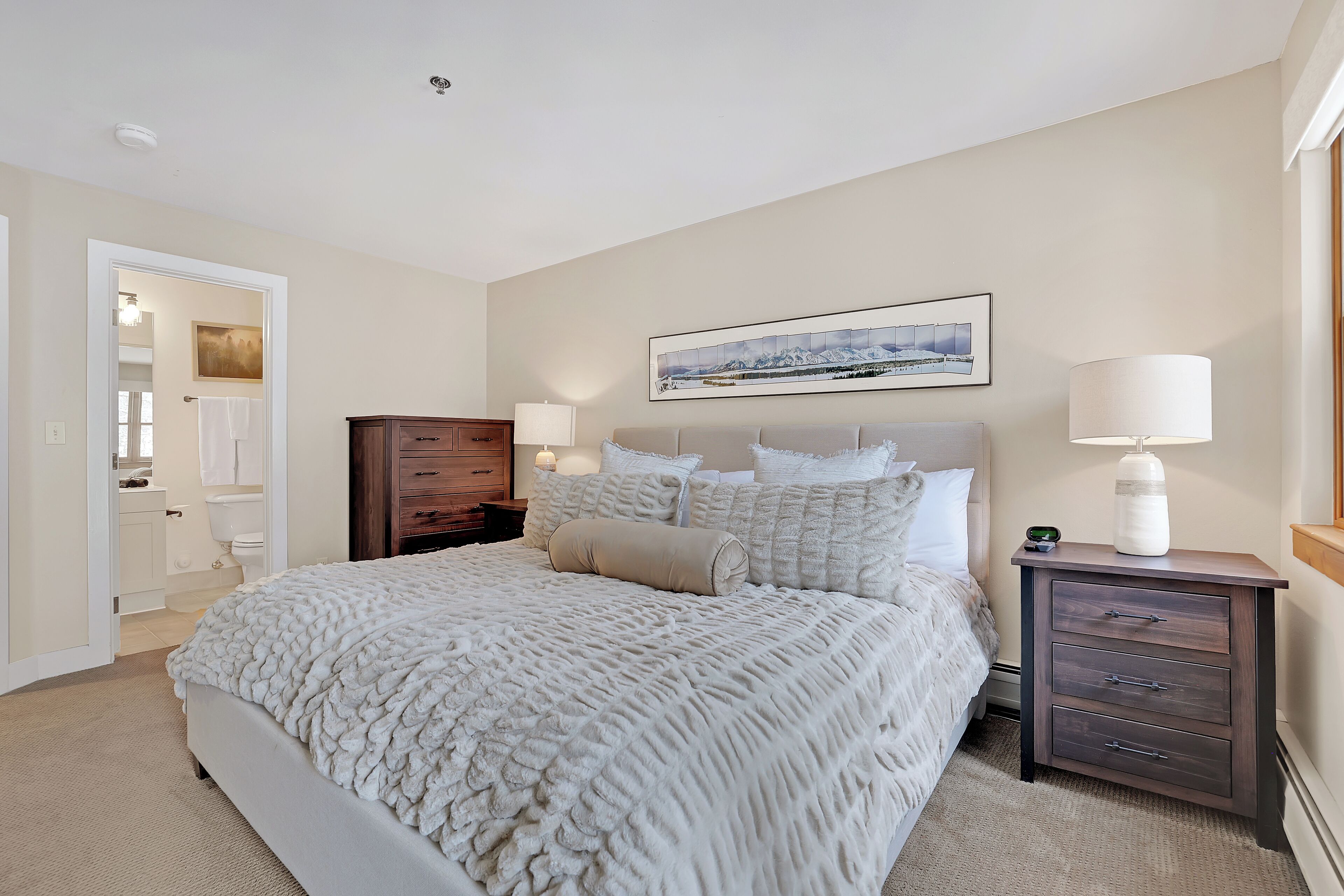 Een slaapkamer met een groot bed, een nachtkastje met een lamp, een dressoir en een schilderij aan de muur.