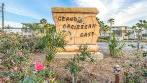Un grand panneau en pierre portant l’inscription « Grand Caribbean East », entouré de plantes en fleurs et d’une clôture.