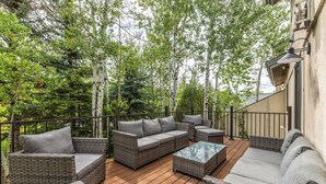 A deck with wicker furniture, including sofas and a coffee table, surrounded by trees.