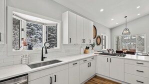 A modern kitchen with white cabinetry, a stainless steel sink, and a window with a view of snow-covered trees.