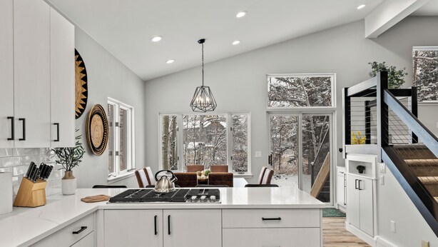 A modern kitchen with white cabinetry, a central island, and a view of snowy trees through large windows.