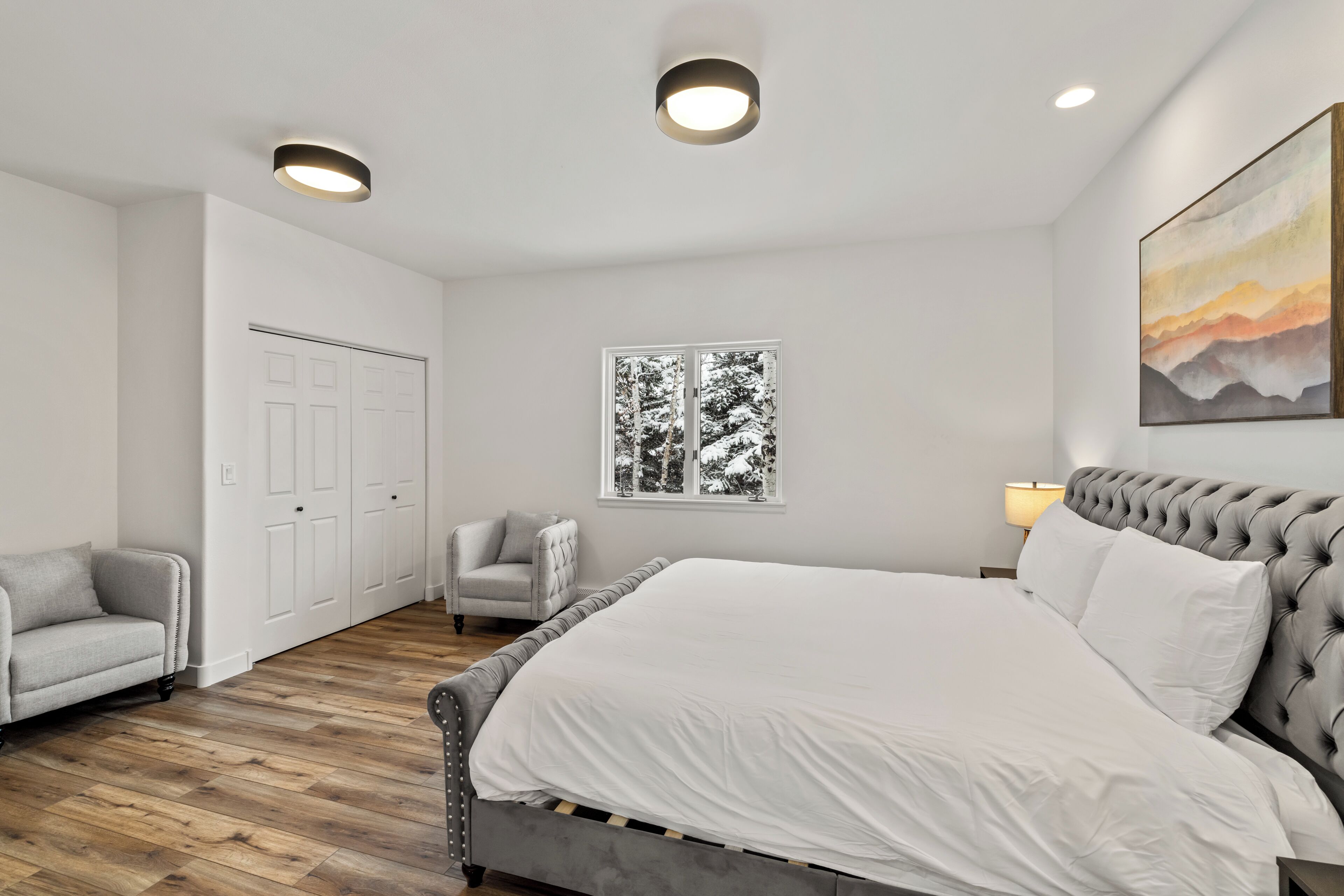 Une chambre à coucher avec un grand lit, une chaise, une armoire et une fenêtre donnant sur des arbres.