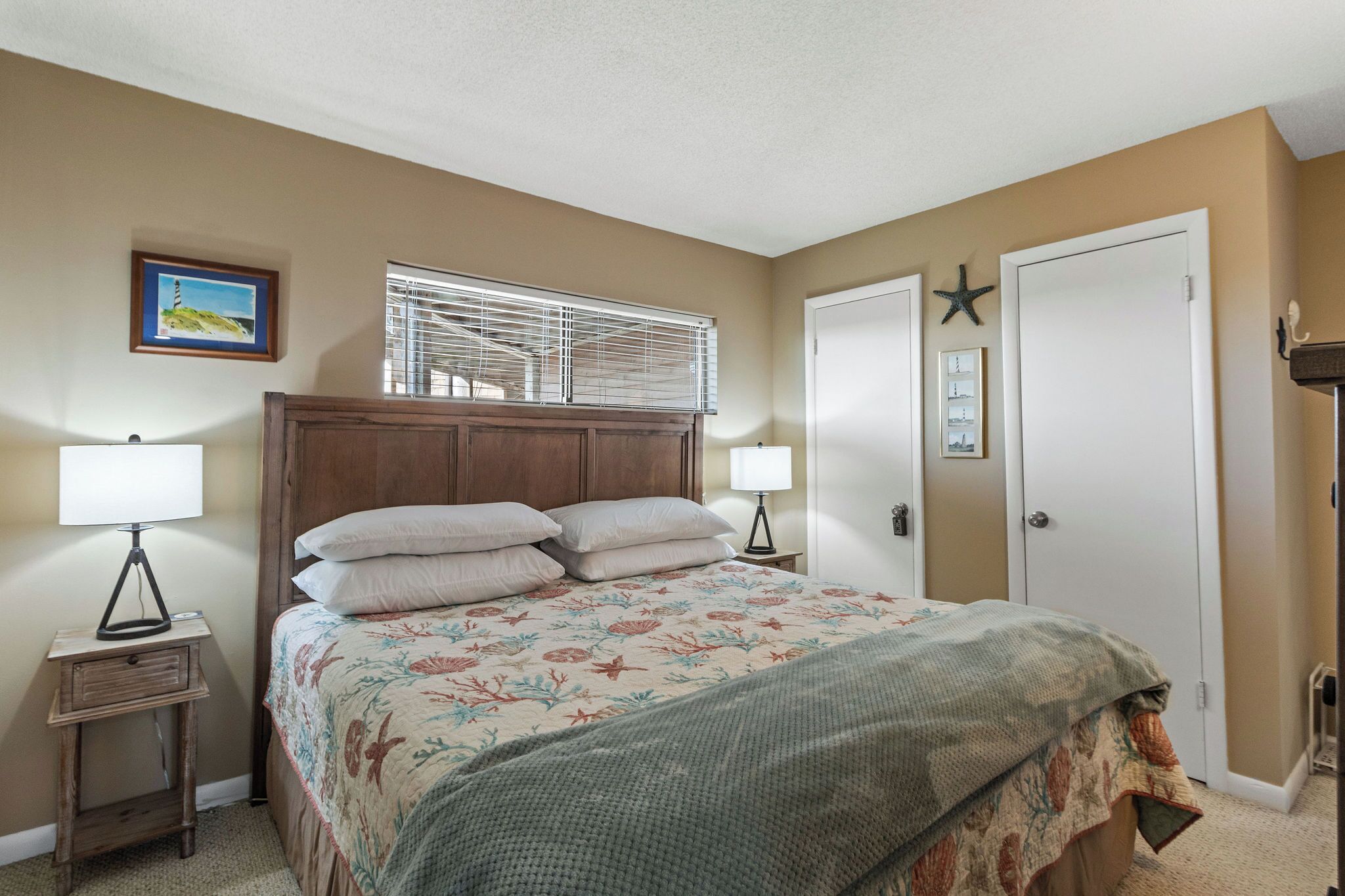 A bedroom with a wooden bed, two bedside lamps, a window with blinds, a framed picture on the wall, and a door with a star decoration.