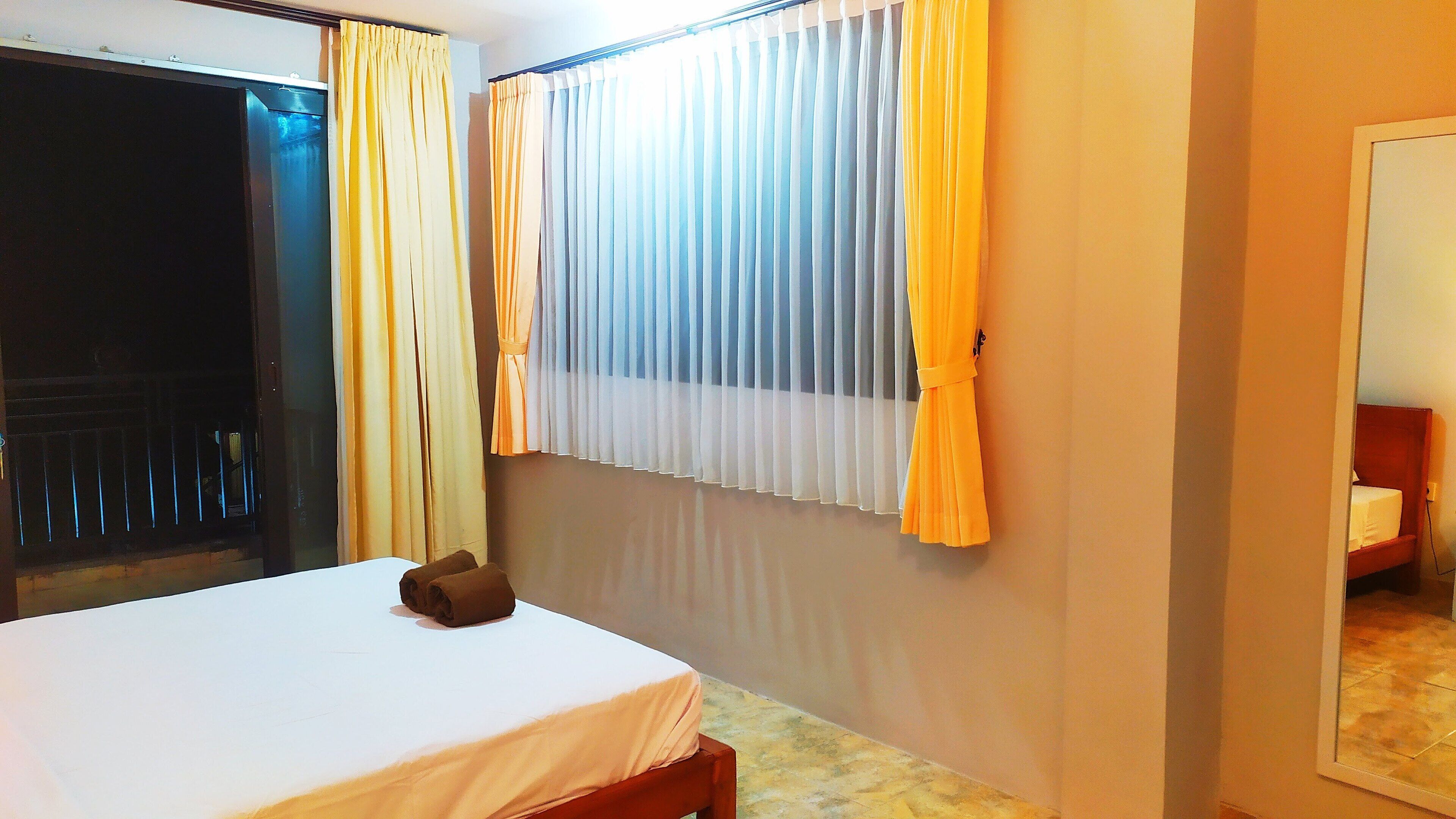 A hotel room with a bed, a window with curtains, a door, and a mirror.