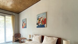 Quarto de hotel com uma cama grande, duas almofadas, mesa de cabeceira com abajur, uma cadeira e dois quadros na parede.