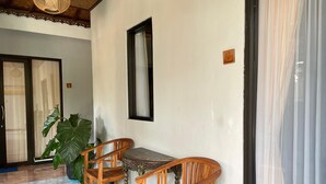 Quarto com mesa de madeira e duas cadeiras, uma planta grande em vaso e uma janela com cortina.
