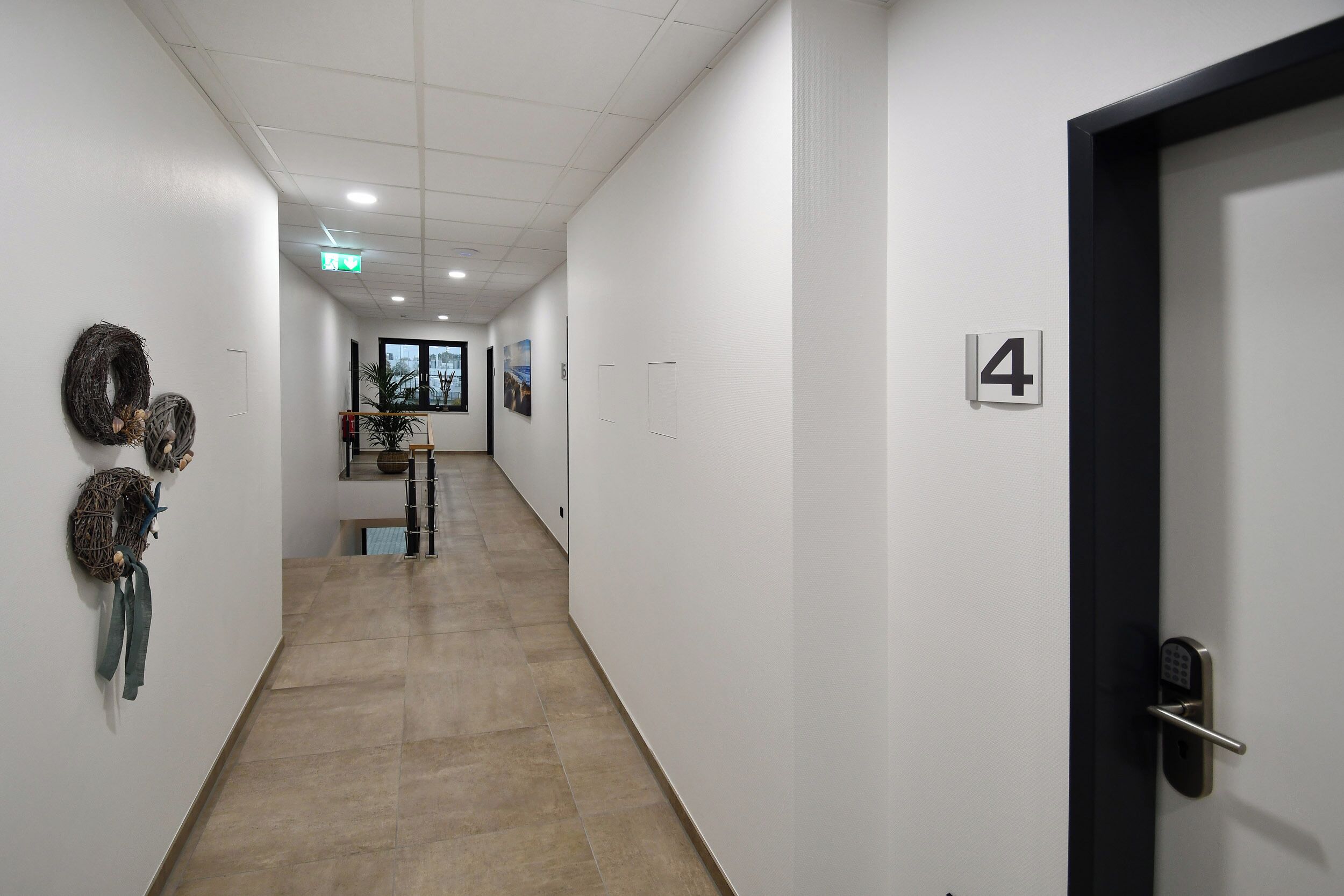 A hallway with a door marked '4', a tiled floor, and wall-mounted decorations including a wreath and a small sign.