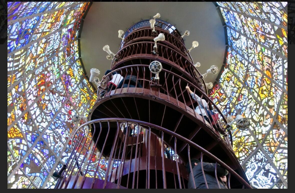 A spiral staircase with a metal railing and a stained glass background.
