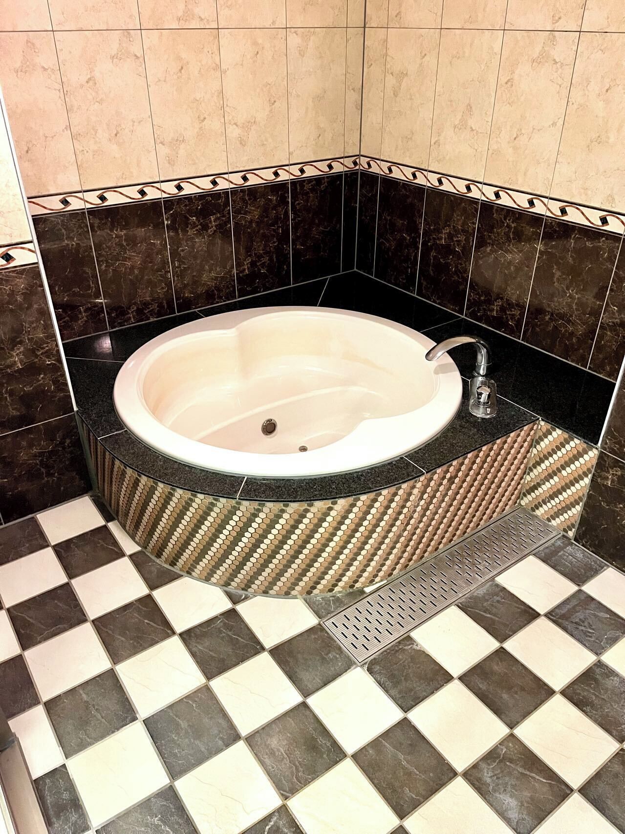 A bathroom with a freestanding bathtub, checkered floor tiles, and dark patterned tiles on the walls.