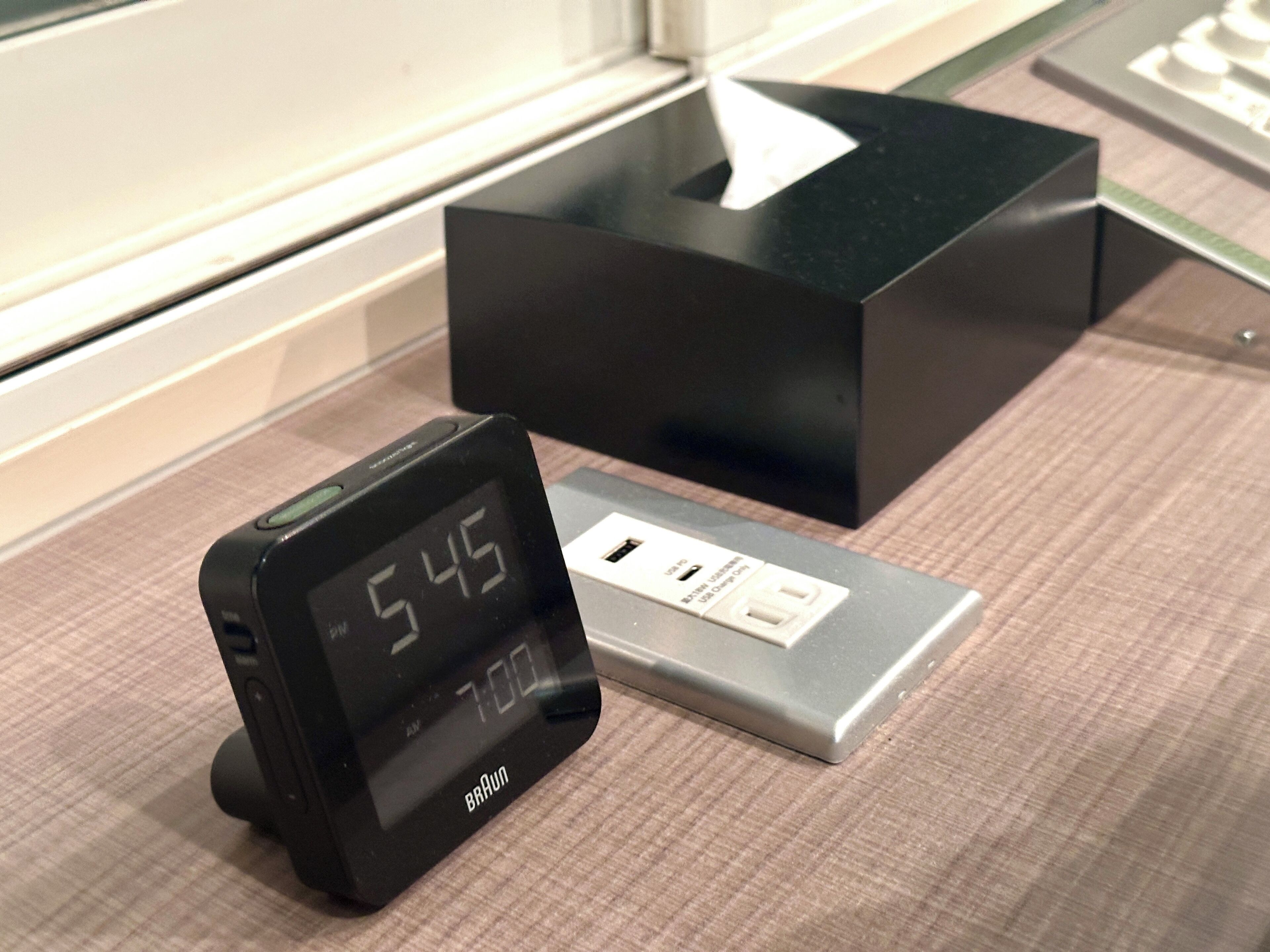 Une horloge numérique affichant 5 h 45 et une station de chargement USB sur une surface à carreaux.