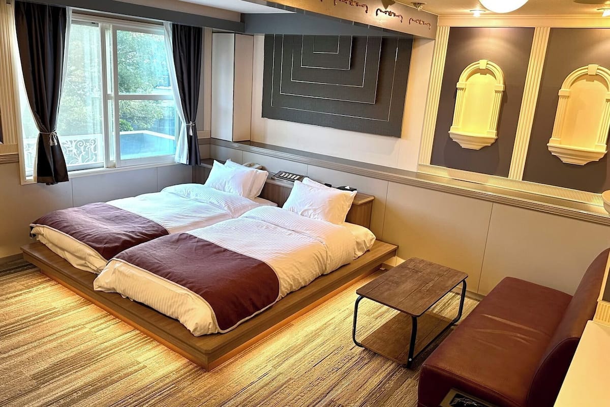 A double bed with a headboard, a small wooden table, a leather armchair, and a window with curtains.