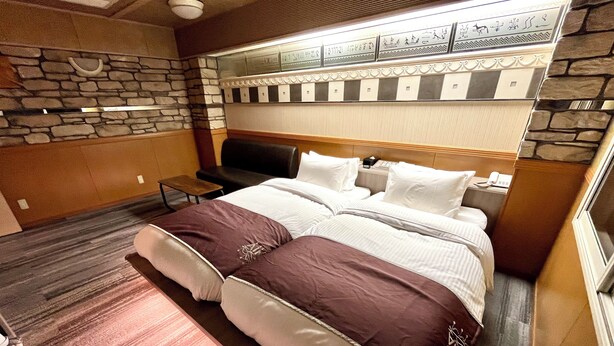 Habitación de hotel con una cama grande, una mesita pequeña y un muro de piedra decorativo.
