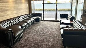 Un área de estar moderna con sofás de cuero, suelo alfombrado, ventanas amplias y vistas al exterior.