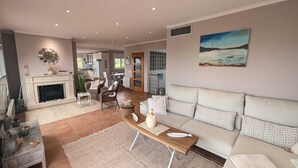 Ein geräumiger Wohnbereich mit Kamin, Sofa, Esstisch und einem Gemälde mit Küstenmotiv.
