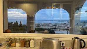 Eine Küche mit Blick auf eine Küstenstadt, einem Toaster, einem Wasserkocher und verschiedenen Gläsern auf der Arbeitsfläche.