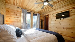 Un dormitorio con paneles de madera, una cama, cortinas, un ventilador de techo y un televisor montado.