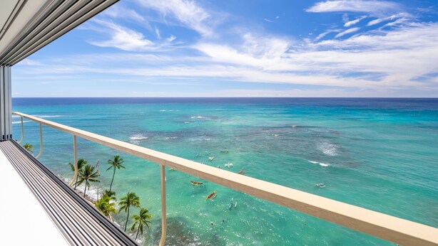 A balcony with a view of turquoise ocean waters and palm trees.