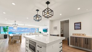 A modern kitchen with a central island, pendant lights, and a view of the ocean.