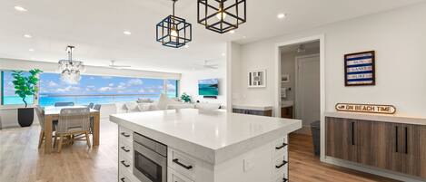 A modern kitchen with a central island, pendant lights, and a view of the ocean.