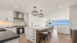 A modern kitchen with a large island, white cabinetry, and a view of the ocean.