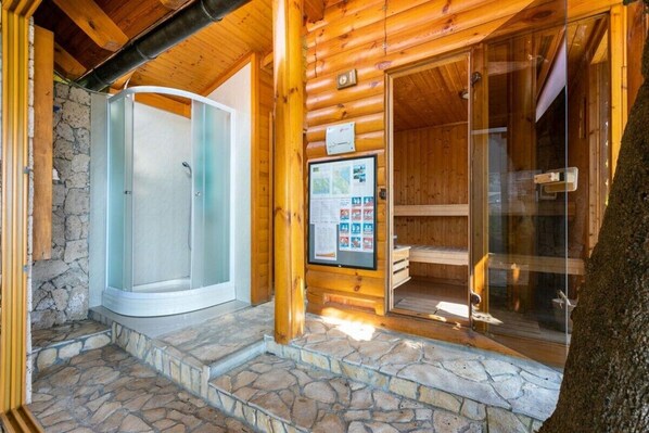 A wooden cabin with a stone exterior, a glass shower enclosure, and a wooden sauna.