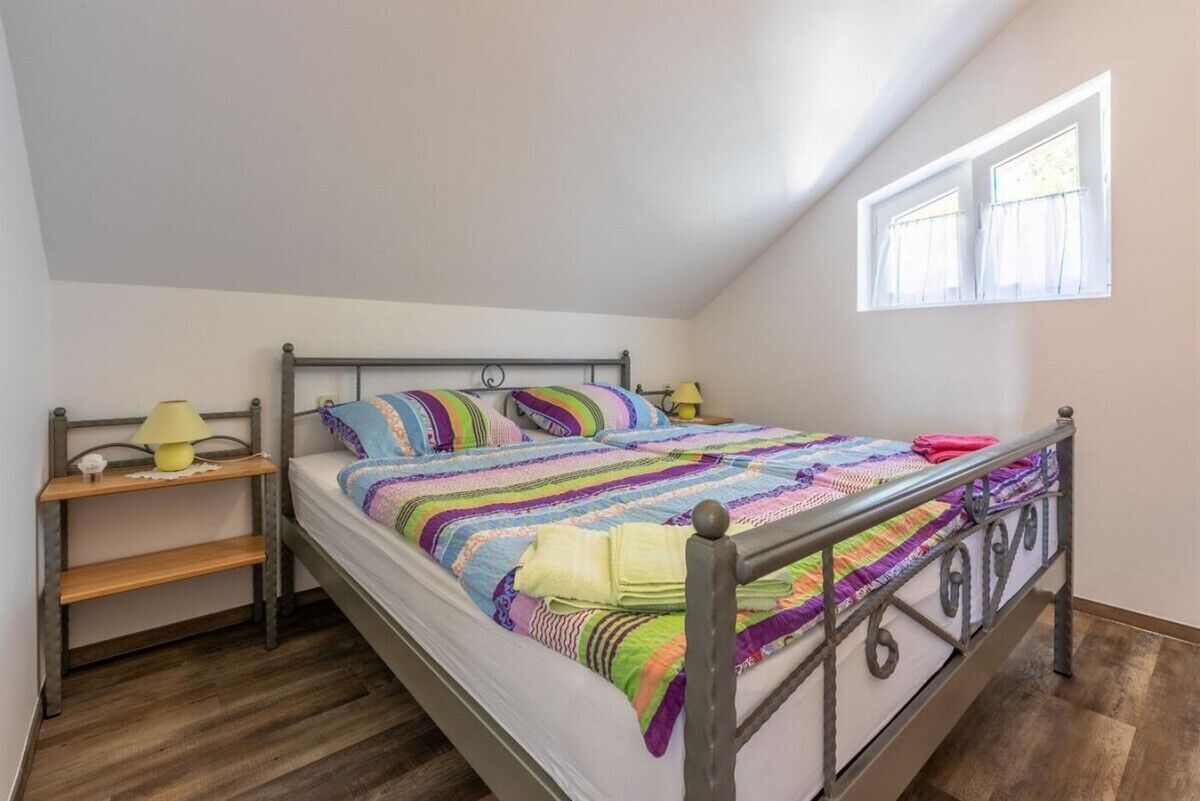 Un lit simple avec un cadre en métal, une table de chevet avec une lampe et une fenêtre avec des rideaux.
