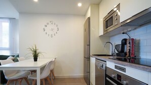 A modern kitchen with a microwave, oven, and dishwasher. There is a dining table with chairs and a potted plant.
