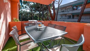An outdoor patio with a metal table and chairs, a barbecue grill, and a view of a building with balconies.