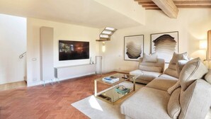 A living room with a large flat-screen TV, a sofa, a coffee table, and abstract wall art. - La Querciola Castelfalfi Borgo (Castelfalfi)