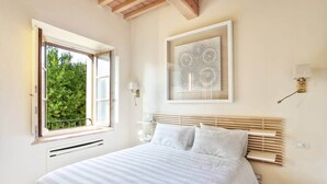 A bedroom with a large bed, a window with a view of greenery, a wall-mounted artwork, and a bedside table with a lamp. - La Querciola Castelfalfi Borgo (Castelfalfi)