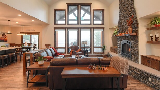 A spacious living room with a large stone fireplace, a dining area with wooden furniture, and large windows allowing natural light. - Spacious 2-Level Custom Craftsman Style Lodge w/ Hot Tub, Fire Pit, Clubhouse (Lead)