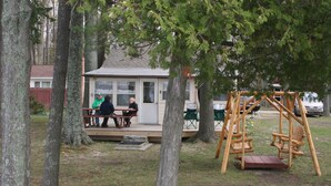 A wooden deck with a swing set and a covered seating area with tables and chairs. - Affordable Family Fun on the Platte Lakes Van Hammen Cottage #3 (Honor)