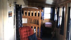 A cozy cabin interior with a wooden bunk bed, a red armchair, and a small table. - Affordable Family Fun on the Platte Lakes Van Hammen Cottage #3 (Honor)
