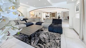 A modern living room with a sectional sofa, a coffee table, and a large white orchid plant. - Family Villa with swimming pool tennis spa (Auribeau sur siagne)