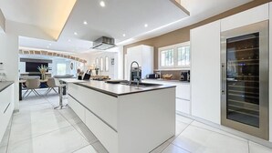 A modern kitchen with a central island, built-in appliances, and a large window providing natural light. - Family Villa with swimming pool tennis spa (Auribeau sur siagne)
