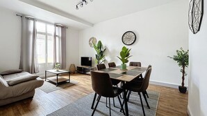 Een moderne woonkamer met een eettafel, stoelen, een bank, een televisie en decoratieve planten.