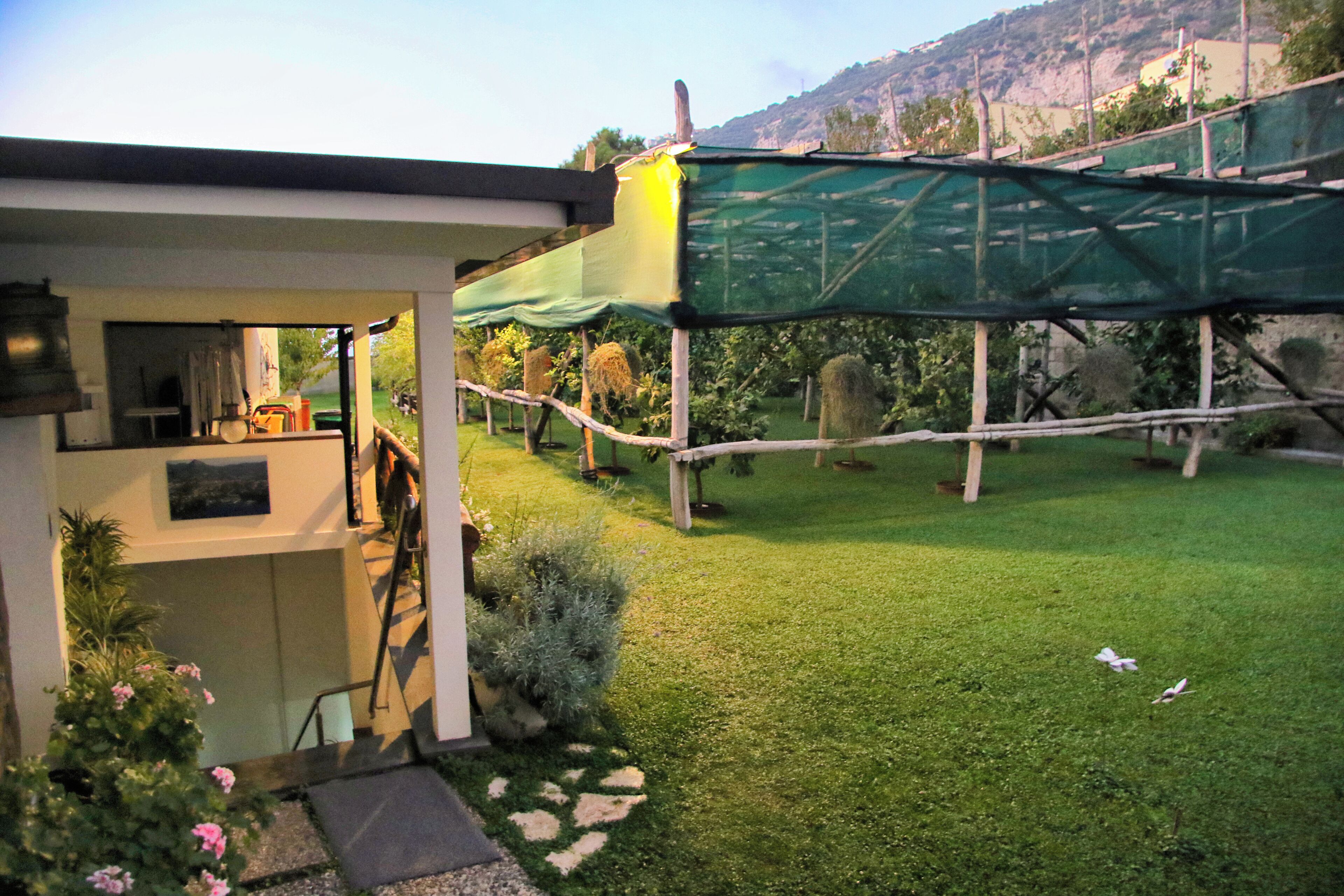 Ein Haus mit überdachter Terrasse, einer Treppe zum Obergeschoss und einem gepflegten Rasen.
