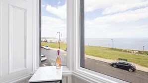A view from a window overlooking a road with cars, a bottle of champagne, and a bench.
