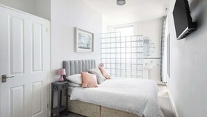 A bedroom with a bed, a bedside table, a lamp, a framed picture on the wall, and a window with a view.