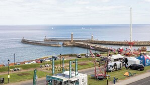 A coastal area with a pier extending into the sea, a lighthouse, and a viewing platform with telescopes.