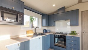 A modern kitchen with blue cabinets, a stainless steel microwave, a gas stove, and a built-in oven. - Host & Stay | Riverwood, Ashdown Retreat (Pickering)