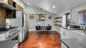 A modern kitchen with stainless steel appliances, a dining table with chairs, and a window with blinds. - Bluebird Day - Lakewood Cottage in Bend with 2 beds, perfect for 4 guests. (Bend)