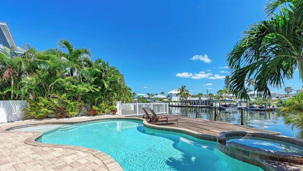A swimming pool with a wooden deck, surrounded by lush greenery and a clear blue sky. - Family-Friendly Waterfront Paradise! (Holmes Beach)